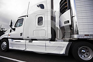 White big rig semi truck with reefer semi trailer and refrigerator unit on it running on the road photo