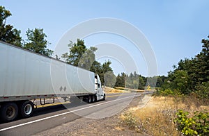 White big rig semi truck transporting cargo in dry van semi trailer on winding green road