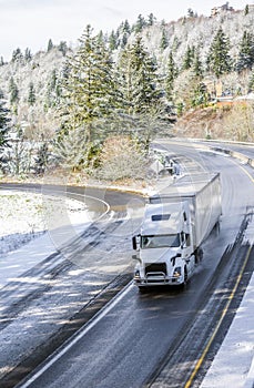 White big rig semi truck transporting cargo in semi trailer driving on winding winter snow road