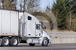 White big rig semi truck transporting commercial cargo in dry van semi trailer running on divided road