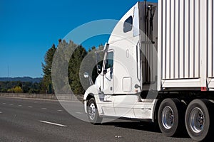 White big rig semi truck transporting container along wide inter