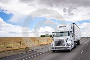 White big rig semi truck transporting food in refrigerated semi trailer moving on wide highway in California
