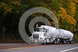 White big rig semi truck with two tank trailers on autumn road