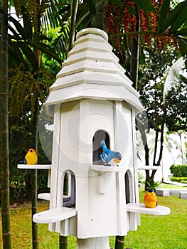 The white bird nest house with a blue bird and two yellow birds, there nestle on a small board at the window. It is decorated in