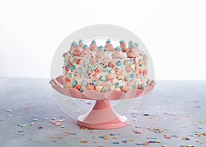 White Birthday cake with pink, blue icing and colorful Sprinkles over a light background with text space. Celebration concept.