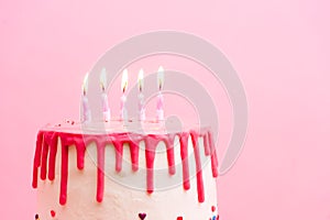 White birthday cake with red chocolate profile on pink background with five colorful lit candles. Happy Birthday party
