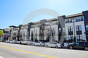 A white and black apartment building with parked cars on the street in front with lush green trees and blue sky in Atlanta