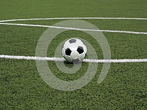 White and black ball for playing soccer lays on green synthetic grass near center of sport playground