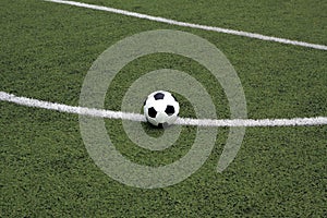 White and black ball for playing soccer lays on green synthetic grass near center of sport playground