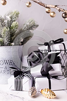 White and black boxes with presents, branches of fir tree in bucket, golden decorative cones