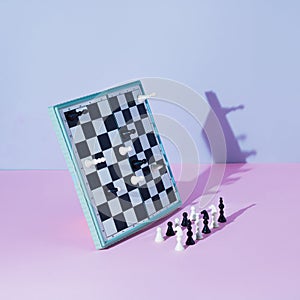 White and black chess board and pieces defy gravity on pink and grey background. Minimal concept