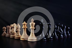 White and black chess pieces against dark background. Competition concept
