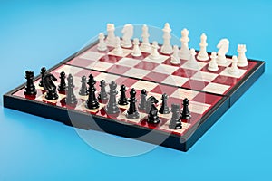 White and black chess pieces placed on a chessboard at the beginning of the game. Blue background. General view
