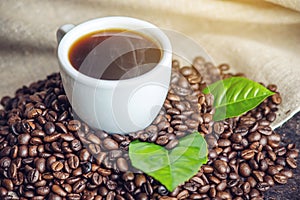 White black espresso Cup with a pile of coffee beans and green leaves in bag on white linen background