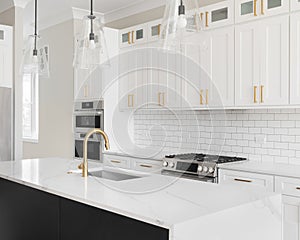 A white and black kitchen with gold accents and subway tile backsplash.