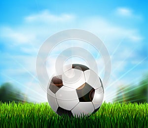 White and black soccer ball on the green glade with grass. Background with blue sky, sunshine and sport equipment for
