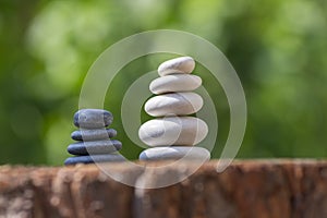 White black stone cairns, poise light pebbles on wood stump in front of green natural background, zen like, harmony and balance