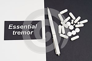 On a white and black surface are pills, a pen and a sign with the inscription - essential tremor
