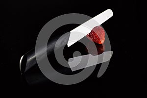 A white blade knife cuts a fresh strawberry and its reflection with black background