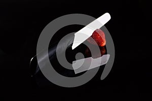 A white blade knife cuts a fresh strawberry and its reflection with black background