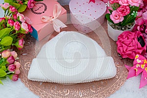 White blank beanie above a small round tablecloth hat surrounded by gift boxes and flowers