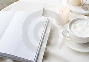 white blank book with cup of coffee and burning candle , cozy composition with opened book mockup