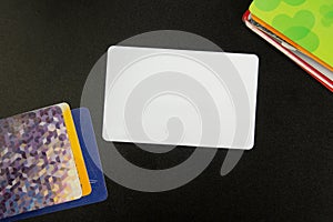 White blank business card. Office desk with set of colorful supplies, cup, pen, pencils, flower, notes, cards on black