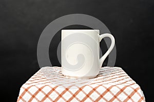 A white blank coffee mug on the top of a hand cloth isolated with black color as the background