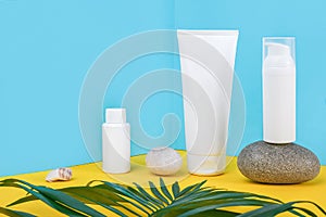 White blank cosmetic tube, bottle with sunscreen, sun cream, moisturizing lotion, rock and green leaf on blue, yellow background.
