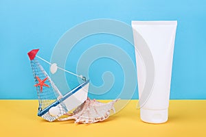 White blank cosmetic tube with sunscreen, sun cream for face or body, seashell and small boat on blue, yellow background. Concept