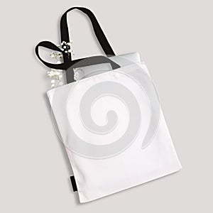 White blank cotton eco tote bag with black straps and little label, laptop and flowers inside. Design mockup