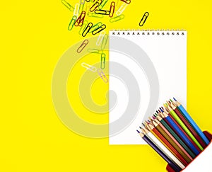 A white blank Notepad in the center and colored pencils with scattered scrapers in the corners