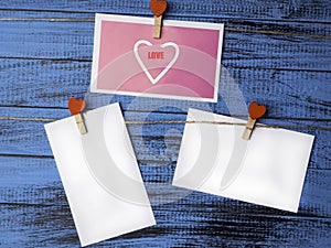 White blank paper sheets on a clothes line and clothespegs with red heart on trendy blue color surface, Valentines day and love