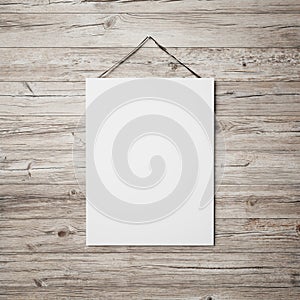 White blank poster hanging on leather belt on wood background