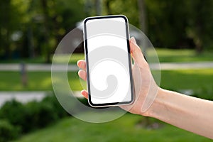 white blank screen mockup cell phone. womans hand holding mobile in park on green blurred background. background empty space for