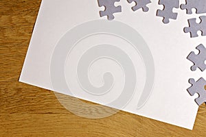 White blank sheet of paper with puzzle pieces on wooden background. Top view. Copy space for text