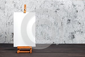 White blank synthetic canvas stretched on subframe and an easel standing on a brown wooden table