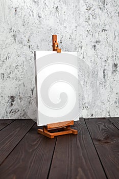 White blank synthetic canvas stretched on subframe and an easel standing on a brown wooden table