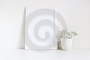 White blank wooden frame mockup with baby breath, Gypsophila flowers in porcelain mug on the table. Poster product photo