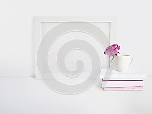 White blank wooden frame mockup with a rose flower in a porcelain cup and pile of books lying on the table. Poster