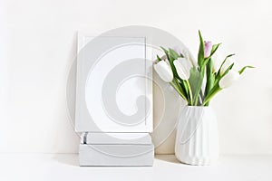 White blank wooden frame mockup with spring bouquet of tulips in porcelain vase and pile of books lying on the table