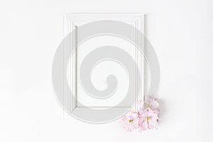 White blank wooden picture frame mockup with pink Japanese cherry blossoms lying on the white table. Poster product