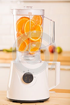 White blender with juicy oranges on a wooden table