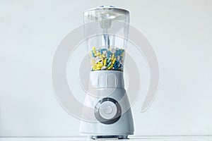 A white blender with multicolored capsules and pills. Nutritional supplementation concept