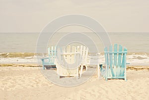 White and blue beach chairs on sand seascape and bright sky in summer vacation relax. Vintage filter tinting, sun haze, glare