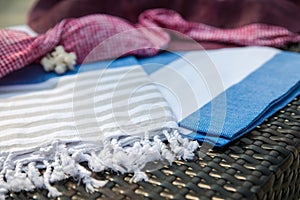 A white, blue and beige Turkish peshtemal / towel, pink bikini top, straw hat and white seashells on rattan lounger as background.