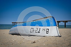White and blue boat flipped on a sandy beach against a blue sky
