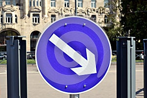white and blue circular metal traffic sign on steel post in closeup view. white directional arrow.