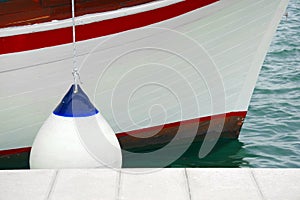 White with blue fender protecting the side of a sailing vessel as it heads into port.