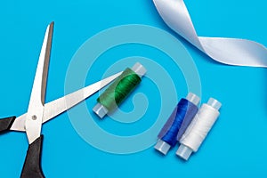 White, blue, green thread and scissors and ribbon on a blue background, copy space, top view